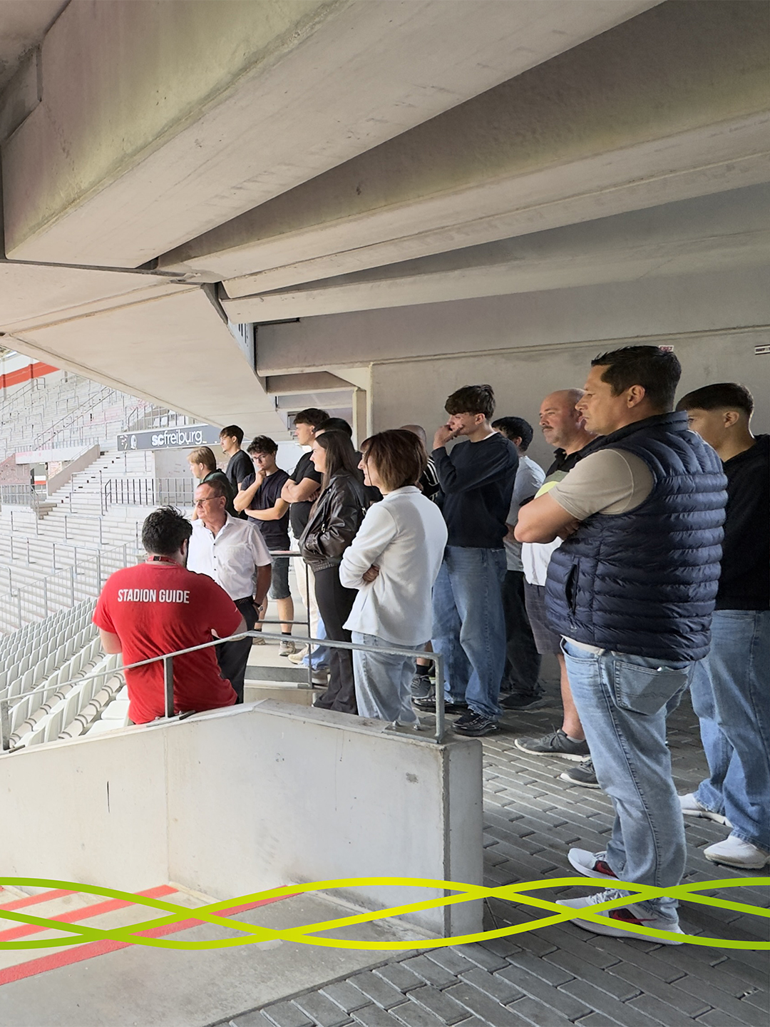 Auszubildende und Begleitpersonen von Badenelektra hören einem Stadionguide bei der Führung durch das Europa-Park Stadion in Freiburg zu.