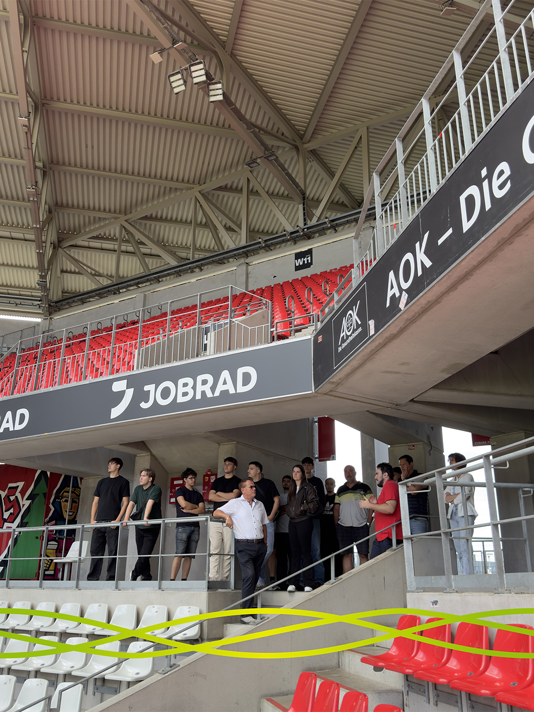 Azubis und Begleitpersonen von Badenelektra bei der Stadionführung im Europa-Park Stadion in Freiburg, während der Guide einen Bereich unter der Tribüne erklärt.