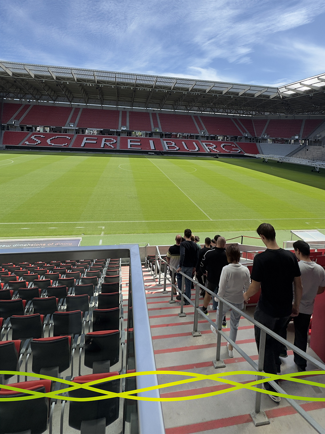Die Gruppe von Badenelektra geht bei der Stadionführung die Tribüne hinunter zum Spielfeld des Europa-Park Stadions in Freiburg.
