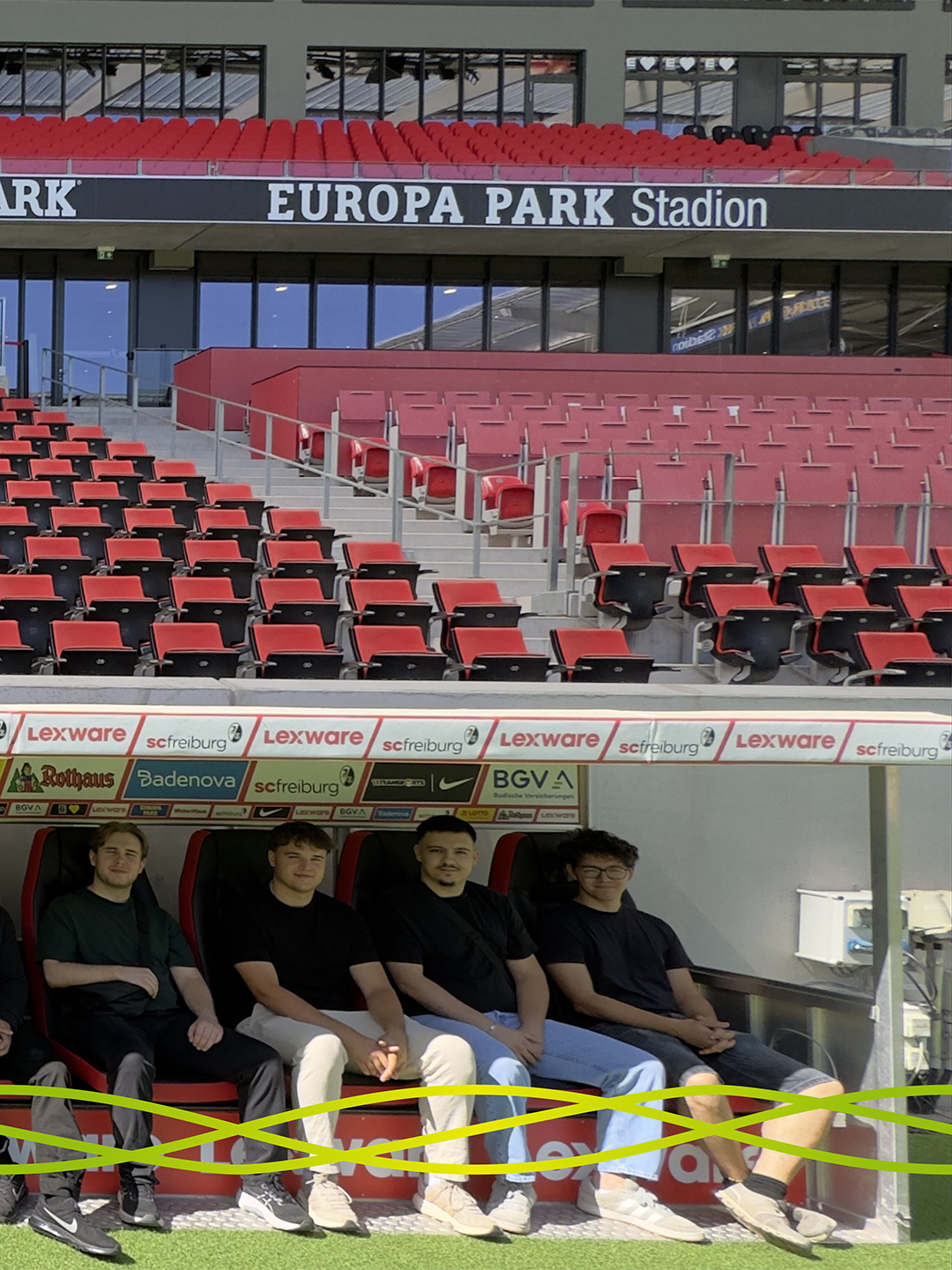 Vier Auszubildende von Badenelektra sitzen bei der Stadionführung auf der Mannschaftsbank am Spielfeldrand des Europa-Park Stadions in Freiburg.