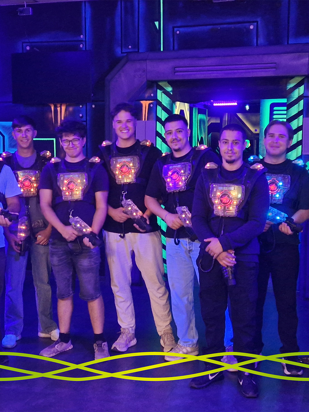 Mehrere Auszubildende von Badenelektra stehen mit Lasertag-Ausrüstung in der farbig beleuchteten Arena der LASERZONE in Denzlingen.