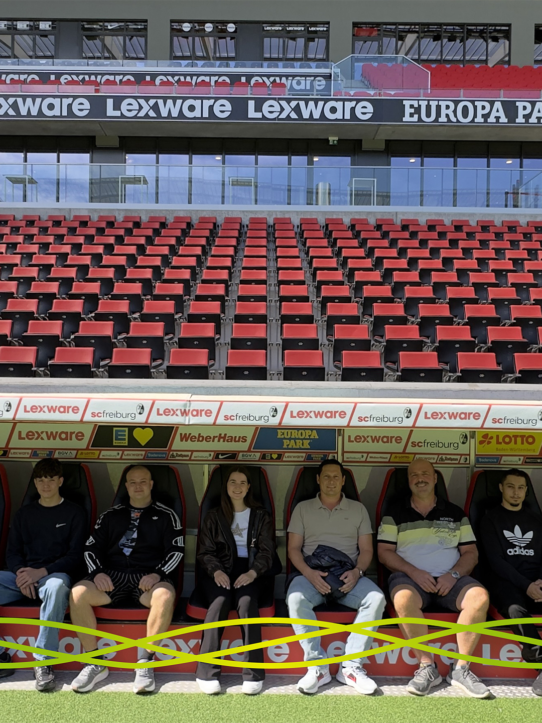 Teilnehmende des Badenelektra-Azubiausflugs sitzen auf der Mannschaftsbank am Spielfeldrand des Europa-Park Stadions in Freiburg.