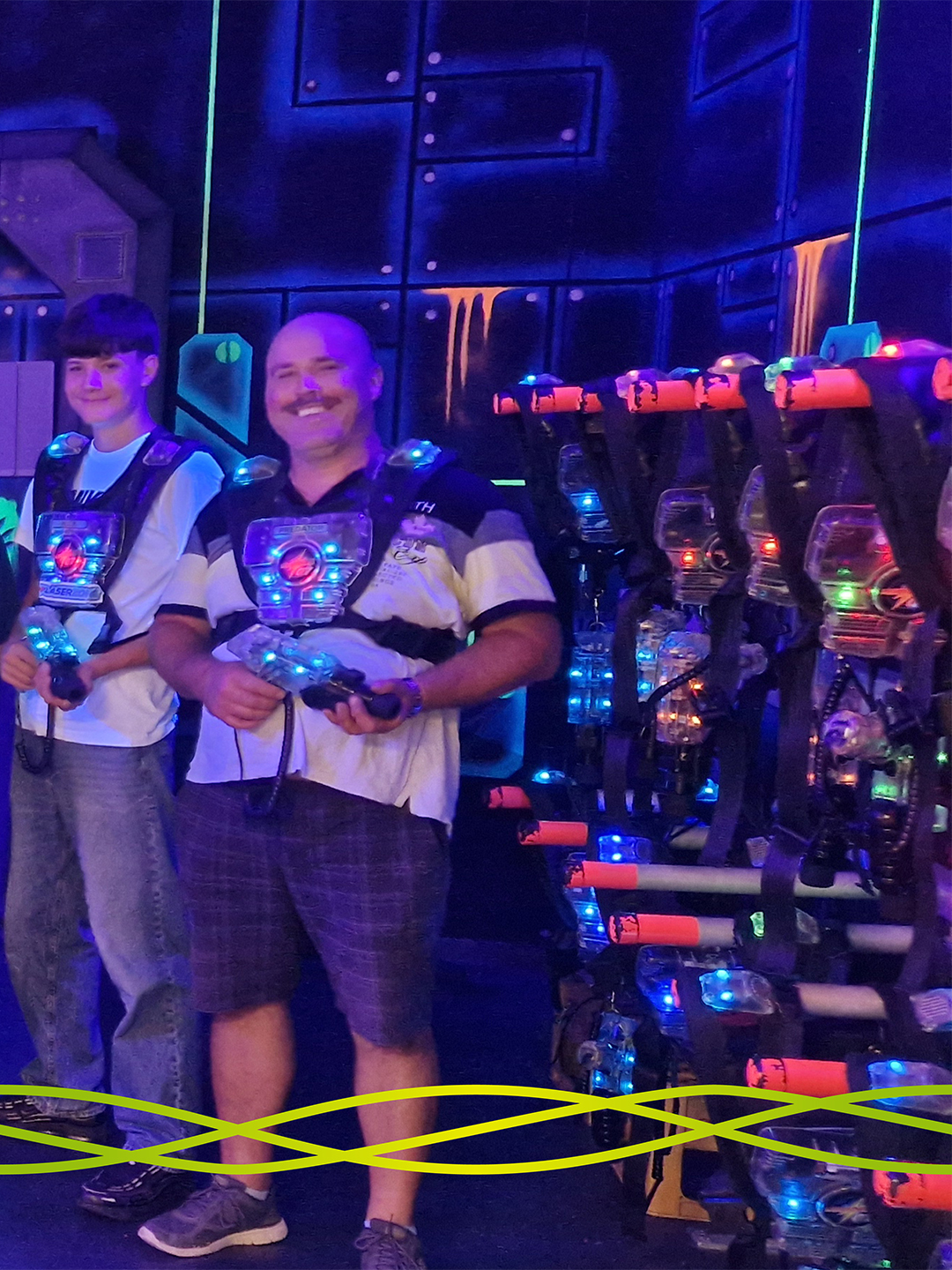 Ein Auszubildender und eine Begleitperson von Badenelektra mit Lasertag-Ausrüstung in der farbig beleuchteten LASERZONE in Denzlingen.